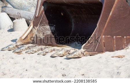 Excavator bucket on sand. Construction equipment on the beach. Heavy construction equipment.