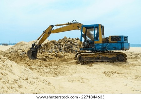 Excavator with a bucket stands on the sand on the beach