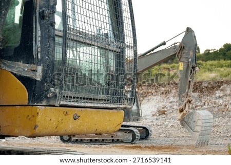 Excavator cab with protective mesh window at the construction site. Symbolizes construction fleet deployment, multiple equipment coordination, safety-first machinery design, and industrial workflows.