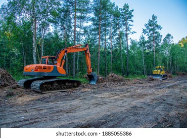 Excavator clearing forest for new development. Orange Backhoe modified for forestry work. Tracked heavy power machinery for forest and peat industry. Logging, road construction in forests