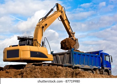 Excavator construction machine loading soil with sand into Tip Truck on blue sky background