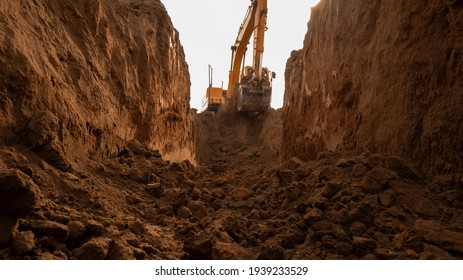 The excavator digs a trench for laying the pipeline. View from the trench. Clay soil. Part of the image is blurred.
