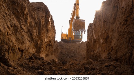 An excavator digs a trench for laying a pipeline. View from the French side. Clay soil. Selective focus.