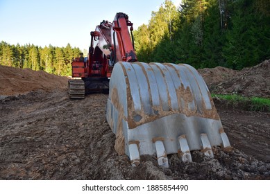 Excavator During Groundwork At Forest Area For Construction New Road. Orange Backhoe On Road Work, Land Clearing, Grading, Excavation, Utility Trenching. Earth-moving Equipment. Open Pit Development