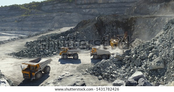 Excavator and heavy\
mining dump trucks in a limestone quarry, loading of stone ore,\
industrial panorama.