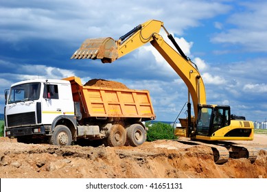 Excavator Loading Dumper Truck Tipper In Sand Pit Over Blue Sky