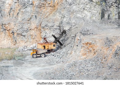 Excavator Is Loading Raw Materials Into Yellow Truck For Transport To Combine. Stone Open Pit.