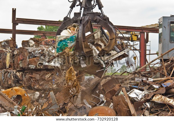 Excavator is loading scrap metal junk\
into a bin at a garbage dump or recycling\
center.