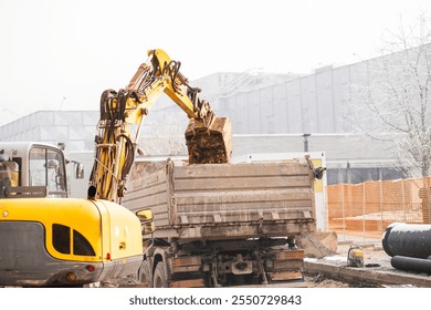 Excavator loading soil into a dump truck on a construction site during the winter season. Snow and frost add to the chilly atmosphere of the urban development project. - Powered by Shutterstock