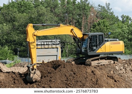 excavator loading soil into dump truck from construction site near forest. selective focus