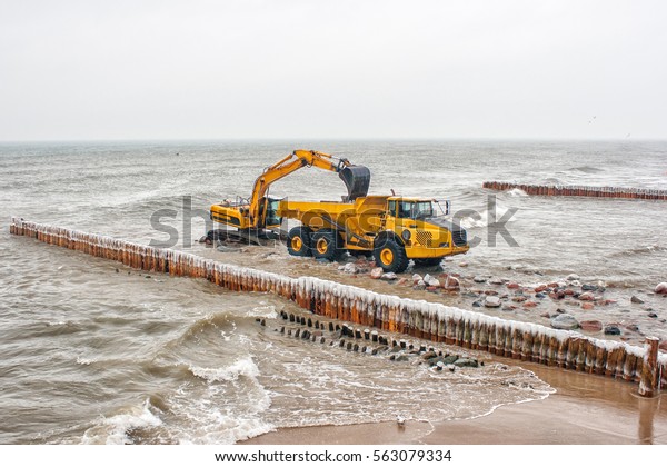 excavator loading a truck stones on the beachon cold\
winter day