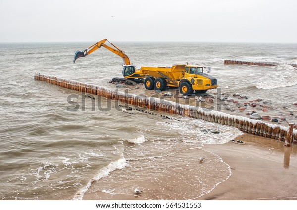 excavator loading a truck stones on the beachon cold\
winter day