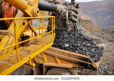 An excavator loads iron ore onto a dump truck in an iron ore quarry. View from the cab of the excavator driver