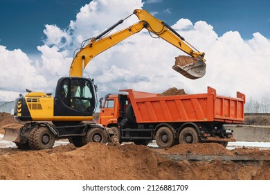 An excavator loads soil or sand into a dump truck. Pit development. Earthworks with the help of heavy construction equipment