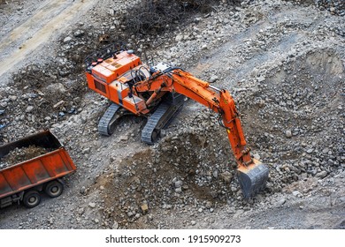 An Excavator Loads Stone Debris Into A Truck. Industrial Land Clearing For Road Construction And Residential Areas. View From Above