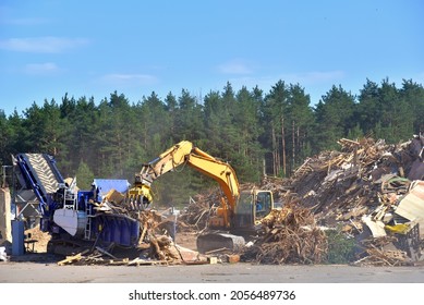 Excavator with log grab crane loads round logs in woodchipper. Mobile chipper for wood chipping. Grab loads timber for lumber mill. Horizontal Grinder and Wood Chipper Shredder. 
 - Shutterstock ID 2056489736