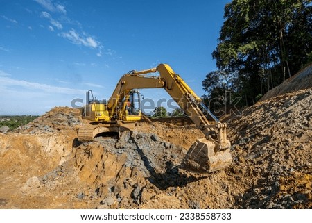 excavator machine activity digging hilly ground with blue sky and banyan tree background