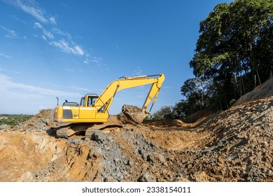 excavator machine at work digging the ground above the hills with forest background and clear blue sky