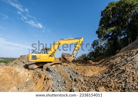excavator machine at work digging the ground above the hills with forest background and clear blue sky