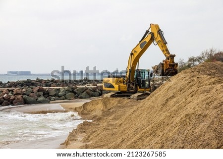 An excavator makes a mound of sand on the seashore. Protection of the beach area for the winter from flooding. Industrial construction equipment and machinery.