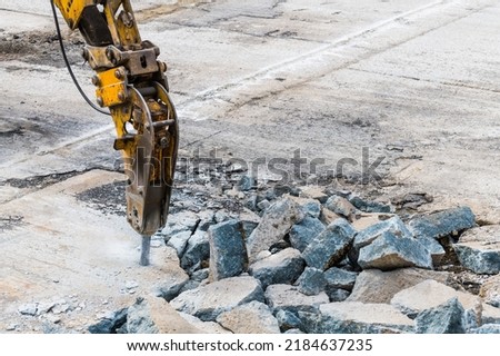 Excavator mounted hydraulic jackhammer at breaking concrete area. Closeup of working demolition hammer with point bit. Heavy equipment detail on construction site. Carpark renewing. Civil engineering.