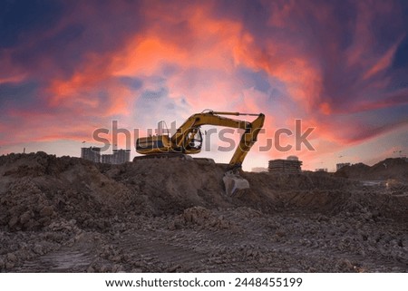 Excavator on earthmoving. Backhoe dig ground on construction site on sunset. Heavy construction equipment on excavation. Tower crane on construction site. Excavator on building groundwork foundation. 
