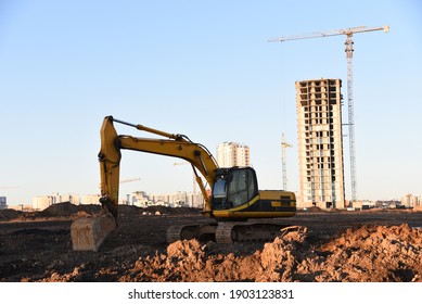 Excavator on earthworks at construction site. Backhoe on foundation work and road construction. Tower cranes in action on blue sky background. Heavy machinery and construction equipment