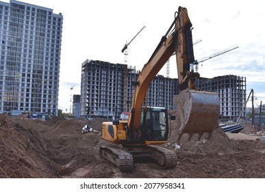 Excavator on earthworks at construction site. Backhoe on road work and laying sewer pipes. Construction machinery for dig ground, excavating foundation. Tower cranes on building construction.