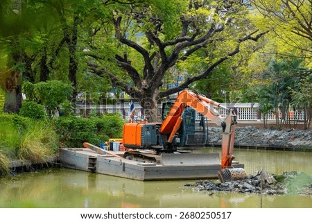 Excavator on floating platform clearing pond in Thailand park.