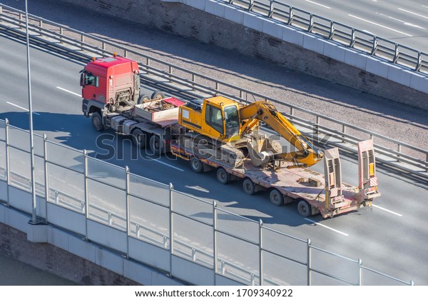 Excavator on transportation\
trailer truck with long trailer platform on the bridge highway in\
the city
