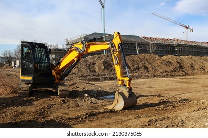 Excavator at work on a dirt area in front of a builing under construction.