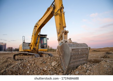 Excavator working at construction site on sunset background. Backhoe digs gravel and concrete crushing. Recycling old concrete from demolition at a landfill for the disposal of construction waste