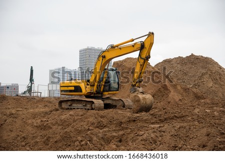 Excavator working at construction site on earthworks. Backhoe digs ground for the foundation and for paving out sewer line. Construction machinery for excavating, loading, lifting and hauling of cargo