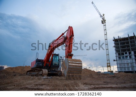 Excavator working at construction site on earthworks on evening sunset. Backhoe digs ground for roadwork. Tower cranes in action construction of a new multi-storey buildings in night