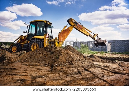Excavator working at house construction site - digging foundations for modern house. Beginning of house building. Earth moving and foundation preparation.