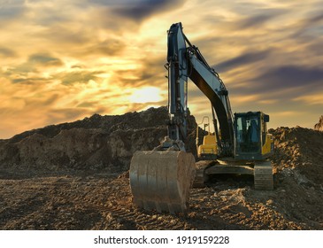 Excavator Working On Earthmoving At Open Pit Mining On Sunset Background. Backhoe Digs Sand And Gravel In Quarry. Heavy Construction Equipment During Excavation At Construction Site