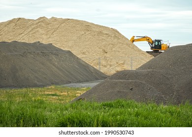 Excavator Works On Different Colored Hills Of Sand, Gravel And Building Materials Under The Blue Sky. Illustration Of Building Industry, Construction Sector Or Mining. Color Photo.        