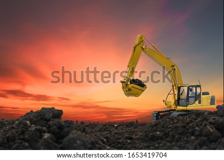 Excavators are digging the soil in the construction site on the orange  sky background