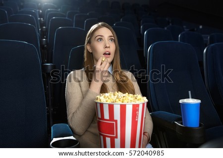 Excellent movie. Young beautiful girl eating popcorn while watching a movie in an empty movie theatre snack holidays entertainment activity alone art enjoy fascination captivating intriguing concept