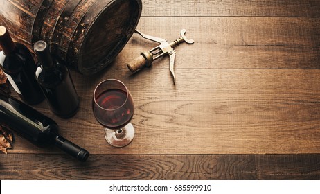 Excellent red wine bottles, wineglass, barrel and corkscrew on a rustic wooden table: traditional winemaking and wine tasting concept