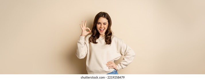 Excellent. Smiling beautiful woman showing okay, ok zero sign, approve smth good, praising and complimenting, beige background. - Shutterstock ID 2219258479