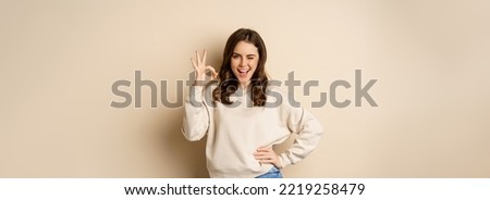 Excellent. Smiling beautiful woman showing okay, ok zero sign, approve smth good, praising and complimenting, beige background.
