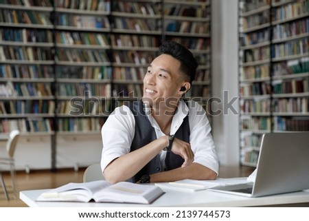 Excellent student, effective e-learn, higher education, professionals skills concept. Handsome Asian guy sit at table in library, distracted from study, prepare for exams, make assignment looks aside