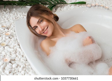 Excelling in care! Tender pretty young model with a charming smile having a soothing bath with foam in the spa salon and posing for camera.