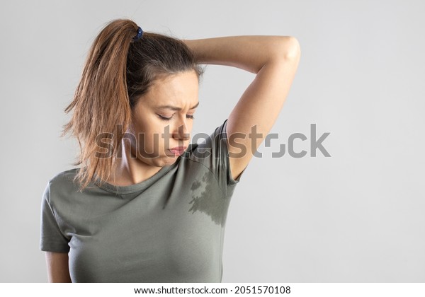 Excessive sweating problems. Young woman with\
her arm raised with her armpits\
sweat.\
