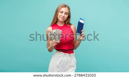 Exchange Learning Concept. Studio portrait of pretty young student woman holding passport with tickets and money. Isolated on bright blue background.