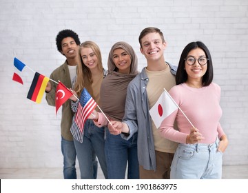 Exchange Students And Language School For Different People. Funny Digital Young International Pupils Holding Flags Of USA, Japan, Turkey, Germany And France In Classroom, Studio Shot, Empty Space