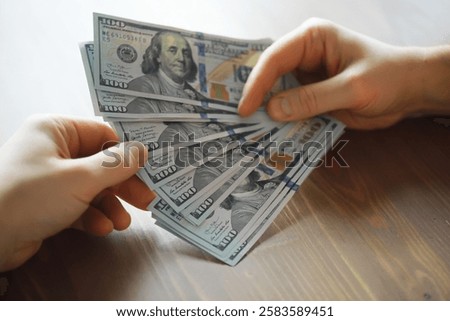 Exchanging Hundred Dollar Bills Between Hands on a Wooden Surface