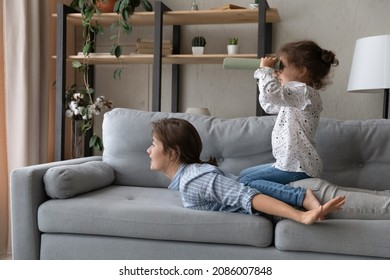 Excited Adorable Daughter Girl Riding Sportive Fit Moms Back, Playing Pirate Sailing Boat, Ship, Looking Through Toy Spyglass. Mum And Kid Enjoying Active Funny Game, Resting On Comfortable Couch