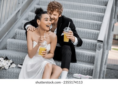 excited african american bride with orange juice laughing near groom on stairs outdoors - Powered by Shutterstock